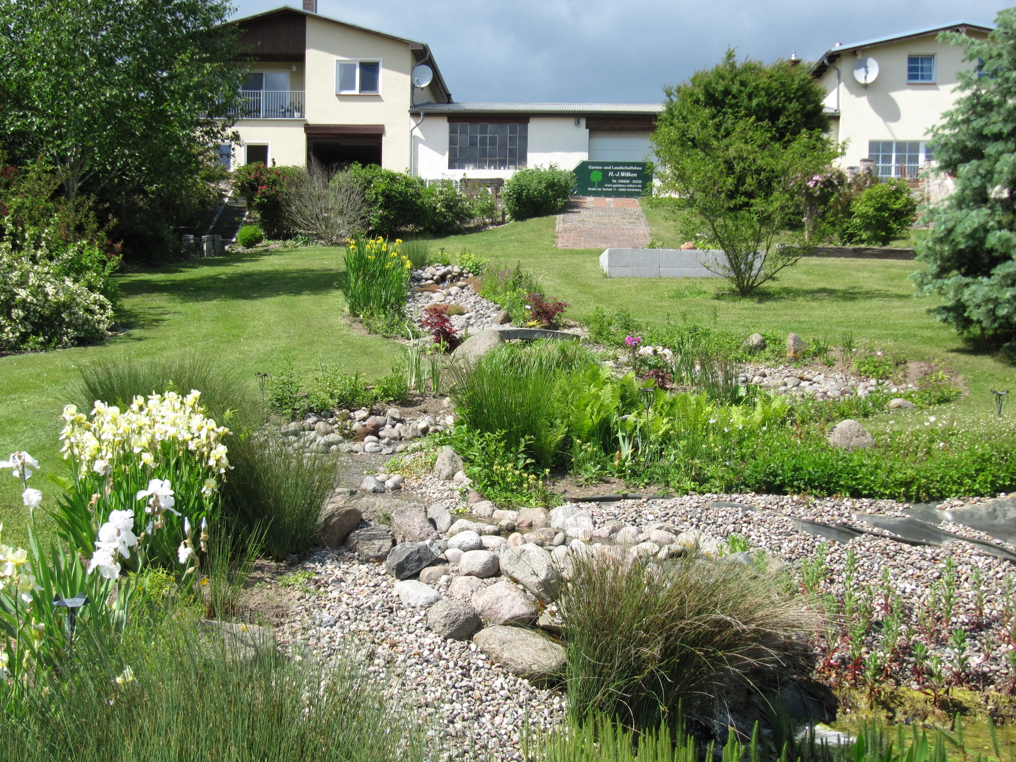 Weitläufige Gartenanlage in Schönberg mit angelegtem Trockenbachlauf, Stauden und Rasen vor einem Wohnhaus