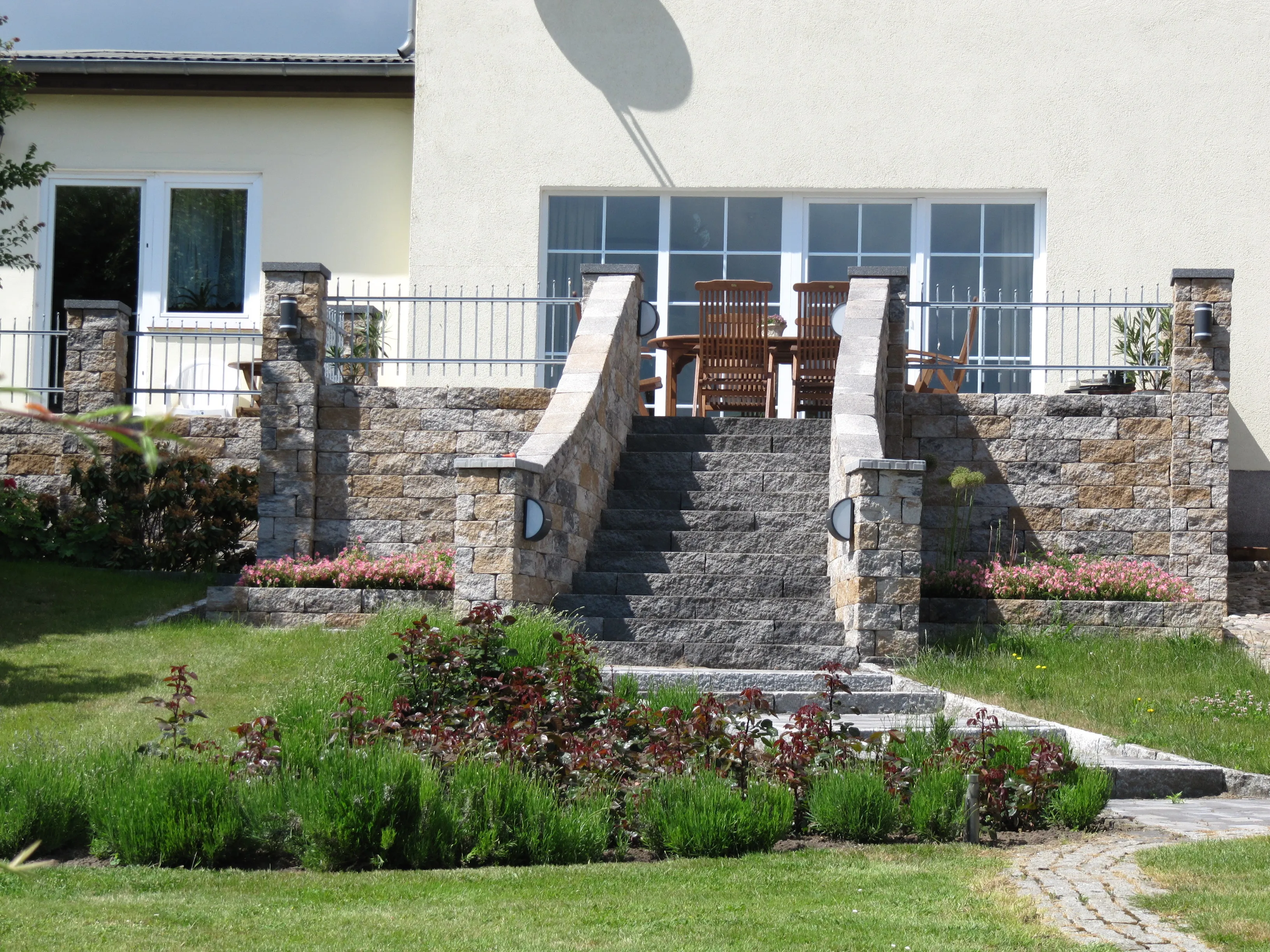 Repräsentative Natursteintreppe mit Geländer und seitlichen Stützmauern vor einem Wohnhaus